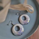 Die weißen runden Boho-Ohrringe punkten durch ihre glänzende Form und die tollen harmonierenden silbernen Glitzerpartikel.  Echte handgefertigte Kunstohrringe.