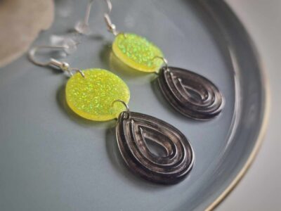 Unter den neongelb glitzernden Kreis-Ohrhängern hängen teiltransparente graue Reliefen-Bögen im herrlichen Komplementär-Look, die Akzente setzen und diese Statementohrringe zu einem individuellen Begleiter machen. 