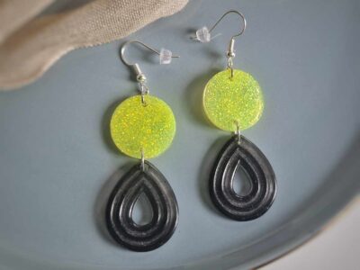 Unter den neongelb glitzernden Kreis-Ohrhängern hängen teiltransparente graue Reliefen-Bögen im herrlichen Komplementär-Look, die Akzente setzen und diese Statementohrringe zu einem individuellen Begleiter machen. 