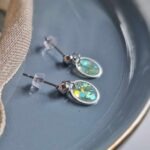 In eine hauchzarte Kreislünette wurde in transparentem Resin pastellgrüne Glitzerpartikel gegossen. Vornehme, handgefertigte Eleganz.