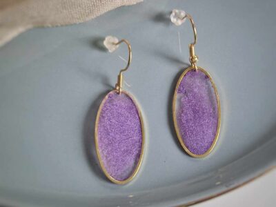 Diese elfenhaften transparenten ovalen Ohrringe in goldener Lünette funkeln und leuchten herrlich in einem pudrigen Violett und sorgen für einen eleganten Auftritt.