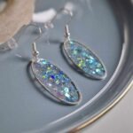 Diese elfenhaften transparenten ovalen Ohrringe in silberner Lünette funkeln und leuchten herrlich durch glitzernde rosa-pastellblaue Pailletten und sorgen für einen eleganten Auftritt.