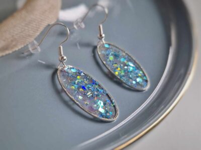 Diese elfenhaften transparenten ovalen Ohrringe in silberner Lünette funkeln und leuchten herrlich durch glitzernde rosa-pastellblaue Pailletten und sorgen für einen eleganten Auftritt.