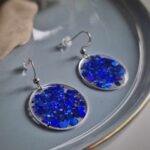 In einer hauchzarten silbernen Kreislünette wurde in das transparente Resin nachtblaue Glitzerpartikeln gegossen, um diese elegante Farbkomposition zu kreieren.