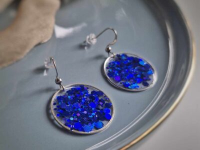 In einer hauchzarten silbernen Kreislünette wurde in das transparente Resin nachtblaue Glitzerpartikeln gegossen, um diese elegante Farbkomposition zu kreieren.