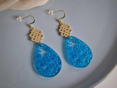 Unter den glänzend-goldenen Mandala-Ohrhängern hängen teiltransparente türkise Orient-Tropfen-Hänger, die diese Ornamentohrringe zu individuellen Begleitern machen.