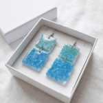 In den transparenten viereckigen-Anhängern wurden glitzernde meergrüne und türkise Herzchen-Pailletten gegossen, die je nach Lichteinfall strahlend leuchten, Akzente setzen und diese Statementohrringe zu  individuellen Begleitern machen.  Echte handgefertigte Kunstohrringe