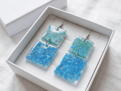 In den transparenten viereckigen-Anhängern wurden glitzernde meergrüne und türkise Herzchen-Pailletten gegossen, die je nach Lichteinfall strahlend leuchten, Akzente setzen und diese Statementohrringe zu  individuellen Begleitern machen.  Echte handgefertigte Kunstohrringe