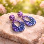 In den transparenten Boho-Anhängern wurden feine glitzernde Pailletten in geheimnisvollen violett und lila Tönen gegossen, die je nach Lichteinfall changierend flieder leuchten, Akzente setzen und diese Statementohrringe zu  individuellen Begleitern machen.