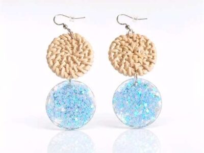 Unter dem hellbeigen Rattankreis baumeln zart gegossene kreisrunde transparente Anhänger mit kleinen glitzernden hellblauen Sternchen, die je nach Lichteinfall changieren.