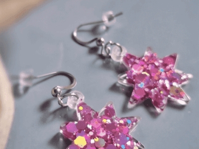 Die hellpinken Stern-Ohrringe funkeln mit changierendem Glitzer und geben eine elegante Optik ab. 30% gehen an den lokalen Tier-und Umweltschutz.