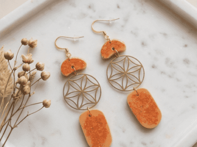 Boho-Ohrhänger „Lebensenergie“ mit Blume des Lebens – OrangeSpüre die harmonisierende Kraft der heiligen Geometrie. Diese kunstvollen Ohrhänger vereinen das kraftvolle Symbol der Blume des Lebens mit der lebendigen Energie von warmem Orange. Die sanft geschwungenen, gesprenkelten Kunstharz-Elemente (Resin) erinnern an organische Kieselsteine und verleihen dem Schmuckstück eine natürliche, erdige Note. Ein absolutes Statement-Piece für Freigeister, das jedem Outfit eine spirituelle und zugleich stilvolle Ausstrahlung verleiht. Handgefertigt für deine Einzigartigkeit.