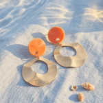 Statement-Ohrringe „Summer Wave“ mit orangem Highlight & GoldSpüre die Wärme der Sonne und das Rauschen des Meeres. Diese ausdrucksstarken Hängeohrringe kombinieren ein kräftiges Orange mit matt-goldenen Elementen, deren wellige Struktur an sanfte Meeresbewegungen erinnert. Perfekt inszeniert im warmen Sonnenlicht, bringen sie Frische und Urlaubsflair in jeden Look. Kombiniere sie mit einem luftigen Leinenkleid für den perfekten Beach-to-Dinner-Style.