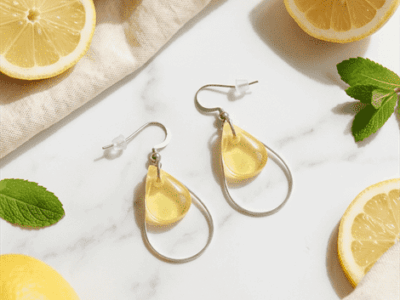 Um die transparent-gelben Anhänger funkeln zarte Edelstahl-Lünetten, die je nach Lichteinfall elegant glänzen und diese Tropfenohrringe zu individuellen Begleitern machen.