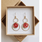 Kunst für deine Ohren! Diese dreistufigen Statement-Ohrhänger vereinen minimalistische Geometrie mit einem aufregenden Farbakzent. Die handgefertigten rot-glitzernden Designkreise bestichen durch ihre einzigartigen, eingearbeiteten Farb- und Metallic-Sprenkel, die an modernes Terrazzo-Muster erinnern. Eingebettet in zwei ineinandergreifende, goldfarbene Ringe entsteht ein dynamischer Look, der bei jeder Bewegung sanft mitschwingt. Ein echtes Unikat für Individualistinnen.
