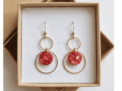 Kunst für deine Ohren! Diese dreistufigen Statement-Ohrhänger vereinen minimalistische Geometrie mit einem aufregenden Farbakzent. Die handgefertigten rot-glitzernden Designkreise bestichen durch ihre einzigartigen, eingearbeiteten Farb- und Metallic-Sprenkel, die an modernes Terrazzo-Muster erinnern. Eingebettet in zwei ineinandergreifende, goldfarbene Ringe entsteht ein dynamischer Look, der bei jeder Bewegung sanft mitschwingt. Ein echtes Unikat für Individualistinnen.