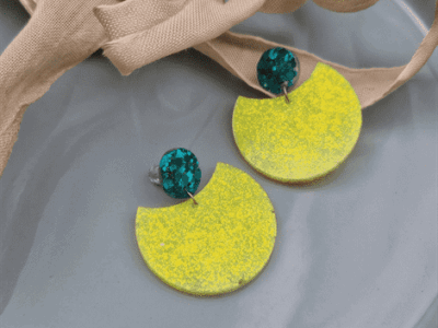 Geometrische Statement-Ohrringe „Neon Breeze“ in Gelb & SmaragdgrünKontraste, die begeistern! Diese auffälligen Hängeohrringe vereinen minimalistische, geometrische Formen mit einer explosiven Farbkombination. Das große, halbkreisförmige Element in leuchtendem Zitronengelb besticht durch seine fein strukturierte Oberfläche. Als eleganter Gegenpol dient der runde Stecker, der mit tiefgrünen Glitzerpartikeln besetzt ist und das Licht faszinierend bricht. Perfekt, um schlichten Outfits im Handumdrehen ein modisches Upgrade zu verpassen.