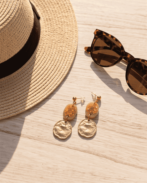 Statement-Ohrringe „Golden Hour“ mit organischen Münzen & Glitzer-DetailsLass dich vom mediterranen Flair verzaubern. Diese luxuriösen Hängeohrringe fangen die magische Stimmung eines Sonnenuntergangs am Strand ein. Das unregelmäßig gehämmerte, goldene Metallelement im Vintage-Stil bildet die perfekte Symbiose mit dem darüberliegenden Glied in warmem Beige-Nude. Der feine, goldene Sternen- und Feinglitzer im Inneren des transparenten Elements reflektiert das Sonnenlicht bei jeder Bewegung. Ein stilvolles Must-Have für edle Sommerkleider, Strohhüte und unvergessliche Sommerabende.