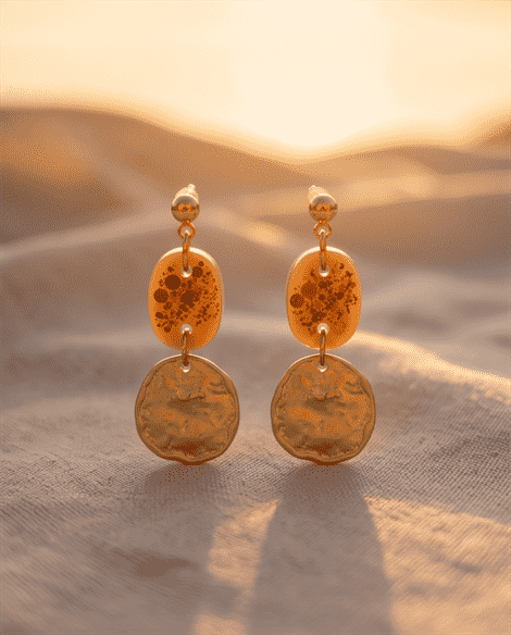 Statement-Ohrringe „Golden Hour“ mit organischen Münzen & Glitzer-DetailsLass dich vom mediterranen Flair verzaubern. Diese luxuriösen Hängeohrringe fangen die magische Stimmung eines Sonnenuntergangs am Strand ein. Das unregelmäßig gehämmerte, goldene Metallelement im Vintage-Stil bildet die perfekte Symbiose mit dem darüberliegenden Glied in warmem Beige-Nude. Der feine, goldene Sternen- und Feinglitzer im Inneren des transparenten Elements reflektiert das Sonnenlicht bei jeder Bewegung. Ein stilvolles Must-Have für edle Sommerkleider, Strohhüte und unvergessliche Sommerabende.