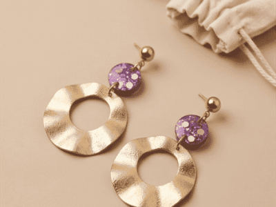 Statement-Ohrringe „Purple Galaxy“ mit gewellten Goldringen & GlitzerLass dich von kosmischer Eleganz verzaubern! Diese ausdrucksstarken Hängeohrringe fangen das Licht bei jeder Bewegung faszinierend ein. Die großen, organisch gewellten Ringe in mattem Goldton bringen eine edle, fließende Dynamik in dein Outfit. Als farbintensiver Blickfang dienen die runden Elemente in tiefem Violett, die mit feinsten holografischen Glitzerpartikeln und Pailletten durchsetzt sind. Ein luxuriöser Hingucker für glamouröse Abend-Looks oder um schlichte Alltags-Outfits stilvoll aufzuwerten.