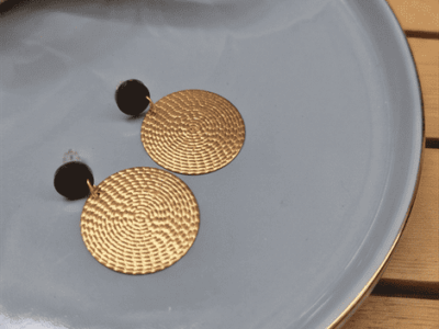 Elegante Statement-Ohrringe „Matinée“ mit strukturierten GoldmünzenEleganz in ihrer reinsten Form. Diese großen, runden Hängeohrringe fangen das Licht durch ihre feine, reliefartige Oberflächenstruktur bei jeder Bewegung elegant ein. Der Kontrast zwischen dem schlichten, mattschwarzen Stecker und dem warmen Goldton des strukturierten Kreises verleiht dem Schmuckstück eine luxuriöse Tiefe. Ein zeitloses Key-Piece, das sowohl das kleine Schwarze am Abend als auch einen cleanen Alltagslook mit Blazer stilvoll aufwertet.