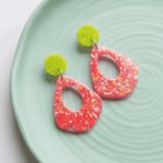Setze ein unübersehbares Highlight! Diese auffälligen Hängeohrringe vereinen moderne Geometrie mit einer erfrischenden, kontrastreichen Farbkombination. Die organischen Anhänger in leuchtendem Pink sind mit zarten, bunten Flakes durchsetzt, die im Licht lebendig schimmern. Als frecher farblicher Gegenspieler funkeln die runden Stecker in spritzigem Neongelb.