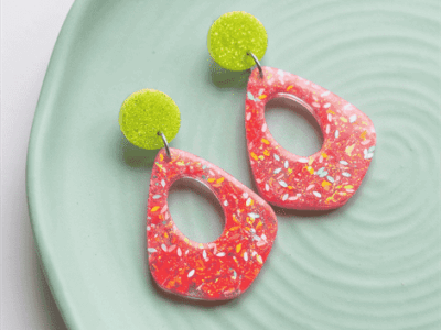 Setze ein unübersehbares Highlight! Diese auffälligen Hängeohrringe vereinen moderne Geometrie mit einer erfrischenden, kontrastreichen Farbkombination. Die organischen Anhänger in leuchtendem Pink sind mit zarten, bunten Flakes durchsetzt, die im Licht lebendig schimmern. Als frecher farblicher Gegenspieler funkeln die runden Stecker in spritzigem Neongelb.