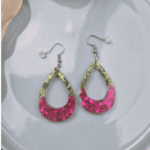 Eleganz trifft auf aufregendes Funkeln! Diese tropfenförmigen Cut-Out-Ohrhänger fangen das Licht bei jeder Bewegung ein und reflektieren es in tiefen Pinklila und Grüntönen. Der fließende Übergang von edlen, gedeckten Glitzerpartikeln im oberen Bereich hin zu der farbintensiven, lila Basis verleiht dem Schmuckstück eine luxuriöse Tiefe.