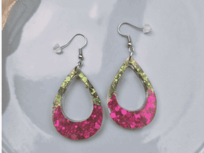 Eleganz trifft auf aufregendes Funkeln! Diese tropfenförmigen Cut-Out-Ohrhänger fangen das Licht bei jeder Bewegung ein und reflektieren es in tiefen Pinklila und Grüntönen. Der fließende Übergang von edlen, gedeckten Glitzerpartikeln im oberen Bereich hin zu der farbintensiven, lila Basis verleiht dem Schmuckstück eine luxuriöse Tiefe.
