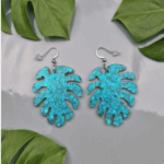 Paradiesische Vibes für dein Outfit! Die ausdrucksstarken Hängeohrringe fangen das Licht bei jeder Bewegung ein. Die filigranen Monstera-Blätter sind gefüllt mit unzähligen türkisfarbenen Glitzerpartikeln und feinen Flakes, die dem Schmuckstück eine wunderschöne optische Tiefe verleihen.