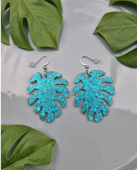 Paradiesische Vibes für dein Outfit! Die ausdrucksstarken Hängeohrringe fangen das Licht bei jeder Bewegung ein. Die filigranen Monstera-Blätter sind gefüllt mit unzähligen türkisfarbenen Glitzerpartikeln und feinen Flakes, die dem Schmuckstück eine wunderschöne optische Tiefe verleihen.