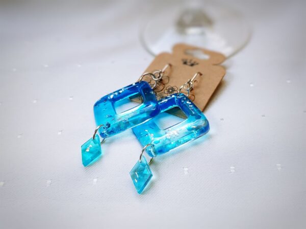 Dieses Paar Resinohrringe wurde in einem transparenten hellen Blau mit funkelnden Elementen gegossen. Ihr Design ist zart und elfenhaft leicht.