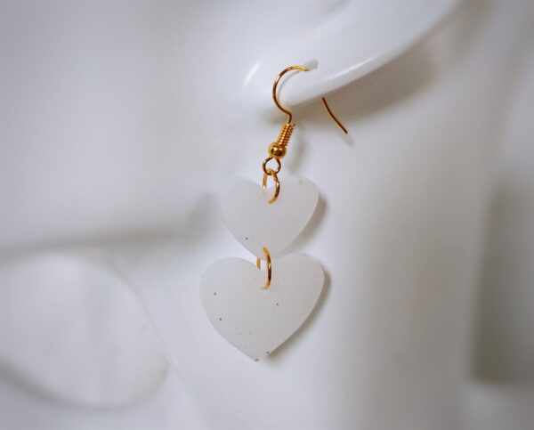 Die handgerfertigten weißen Resinohrringe weisen eine schillernde Struktur auf und wirken dank ihrer Herzform gleichermaßen verspielt, wie romantisch.