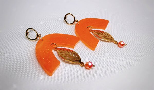 Die handgerfertigten herbstlichen Ohrringe aus Kunstharz sind in einem satten Orangeton mit schimmernden Nuancen gehalten. Ein Gold glänzendes mittig platziertes Blatt wippt wie Herbstlaub im Wind mit.