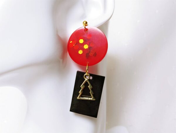 Für alle, die an Weihnachten nicht auf außergewöhnliche Accessoires verzichten möchten, gibt es dieses Special Ohrringpaar in einem rechteckigen Schwarz mit goldenen Tannenbaum davor und mit Pailletten versehehen weihnachtsmannroten Kreisen.