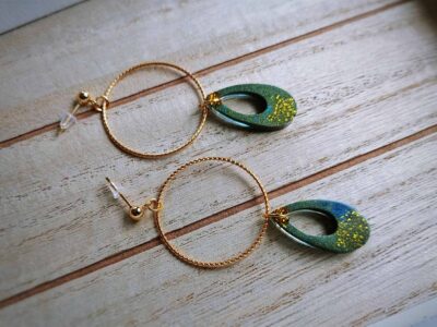 Diese zarten Art Decó Ohrhänger in schimmerndem Olivgrün mit Glitzerpartikeln bezaubern durch ihre filigrane Strukturen und die feinen goldenen Kreisanhänger.