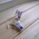 Diese zierlichen Ohrhänger zeigen sich von ihrer spritzigen Seite und präsentieren einen lila Cocktail á la "Purple Rain" im Glas.