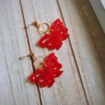 Unter einem filigranen, gold glänzenden Kreis fliegen zarte rote Schmetterlinge und machen diese romantischen Ohrringe zu wahren Hingucker.