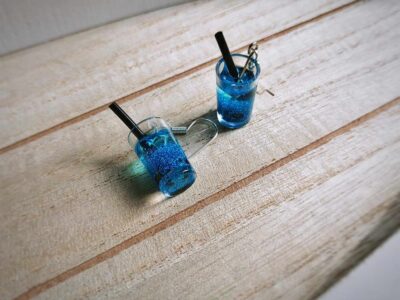 Diese zierlichen Ohrhänger zeigen sich von ihrer spritzigen Seite und präsentieren einen blauen Cocktail á la "blaue Lagune" mit Eiswürfeln im Glas.