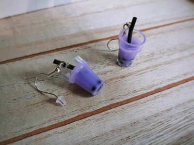 Diese zierlichen Ohrhänger zeigen sich von ihrer spritzigen Seite und präsentieren einen Bubble Tea mit lila Inhalt im Glas.
