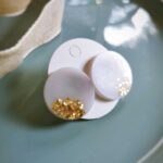Diese handgefertigten flachen runden Ohrstecker setzen auf eine dezente Weise Akzente und überzeugen durch ein edles Emailleweiß mit goldenem Glimmer.