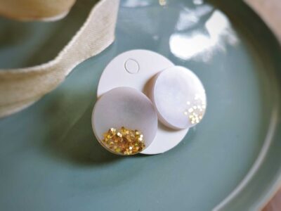 Diese handgefertigten flachen runden Ohrstecker setzen auf eine dezente Weise Akzente und überzeugen durch ein edles Emailleweiß mit goldenem Glimmer.