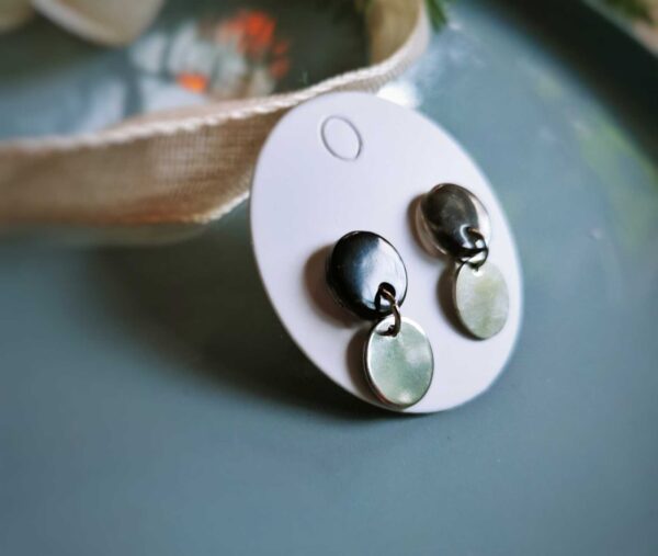 Diese handgefertigten runden schwarz-transparenten Ohrstecker setzen auf eine dezent-elegante Weise Akzente und überzeugen durch elegant schimmernde kleine silberne Metallhängerchen.